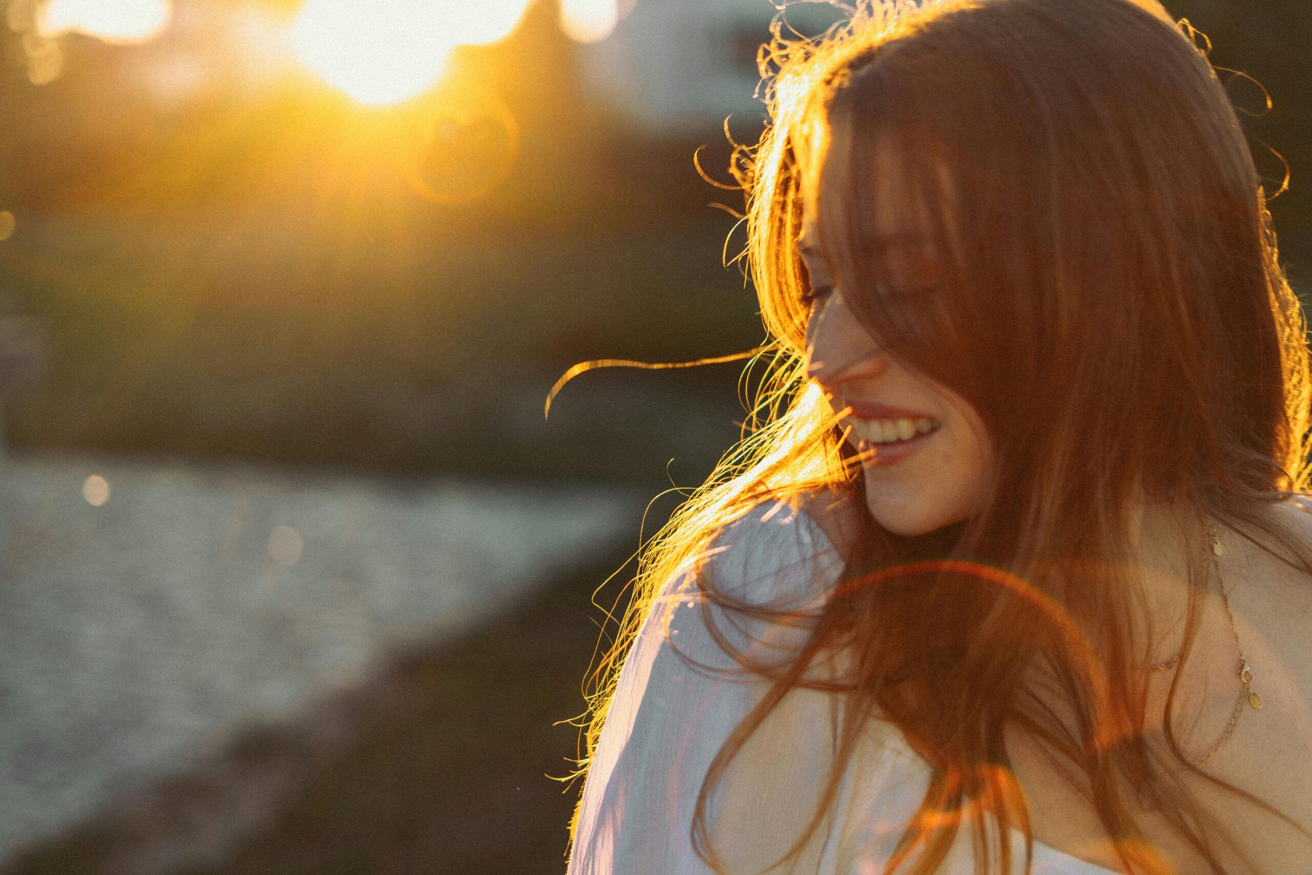 Woman enjoying sunset with a radiant smile and soft light in outdoor setting.